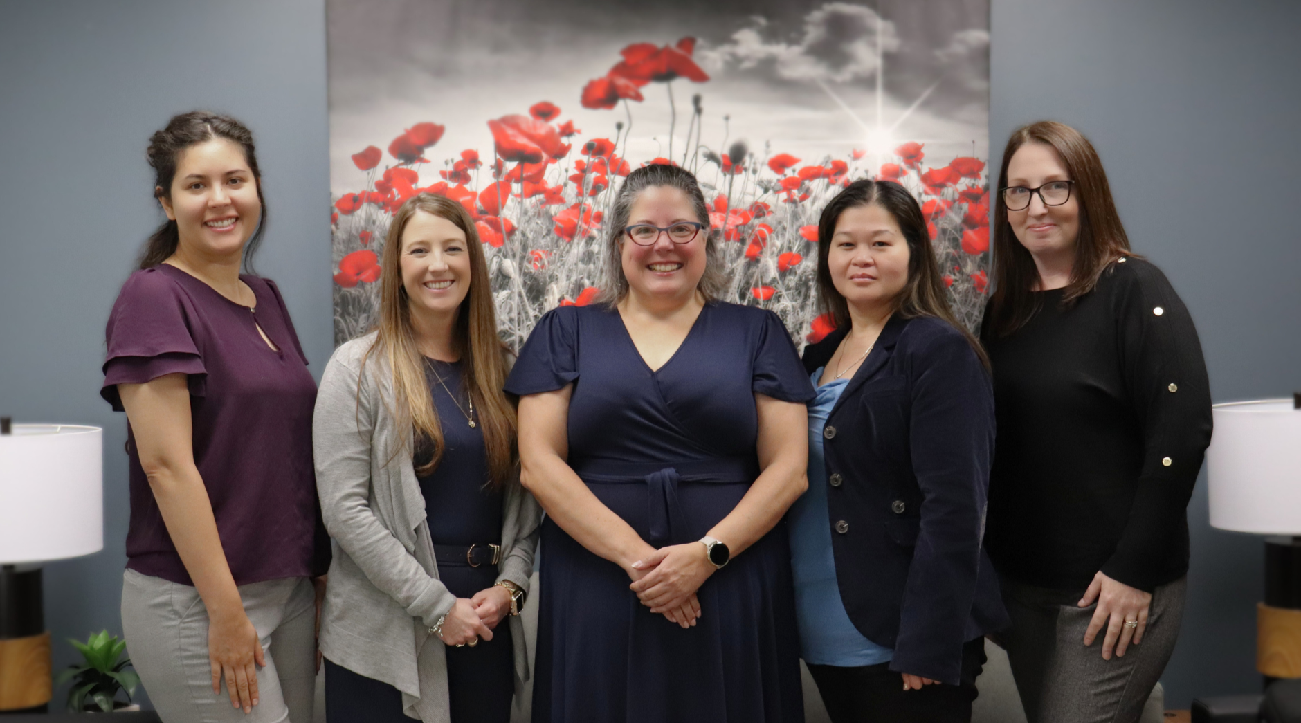A group of 5 people stand together in front of a backdrop of poppies.